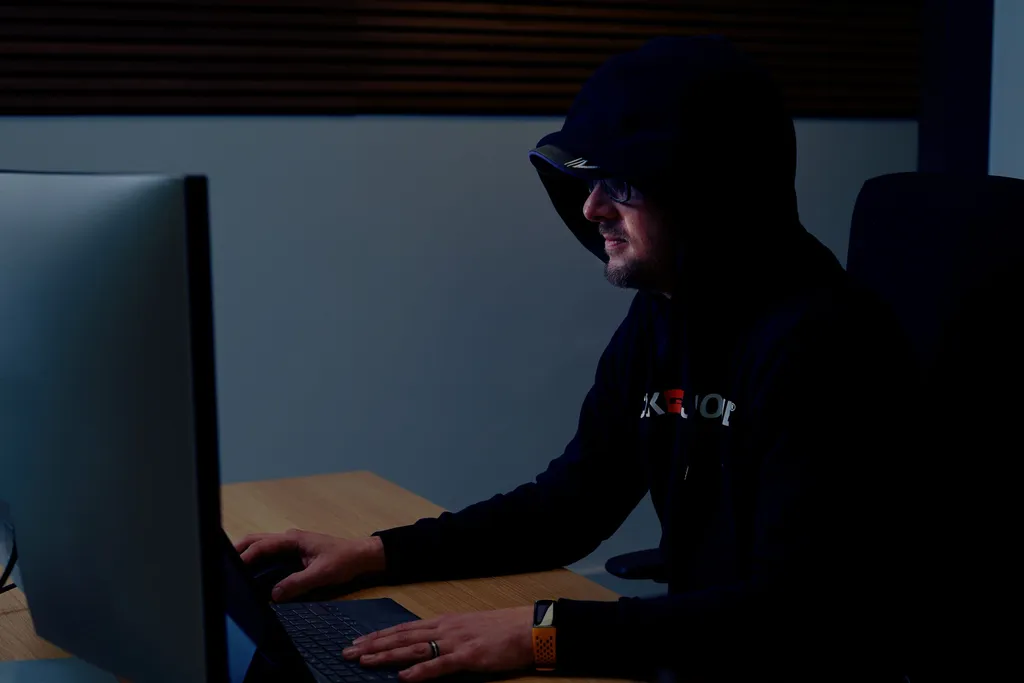 Person with a Dark Hoodie working on a computer in a dark room symbolizing a hacker