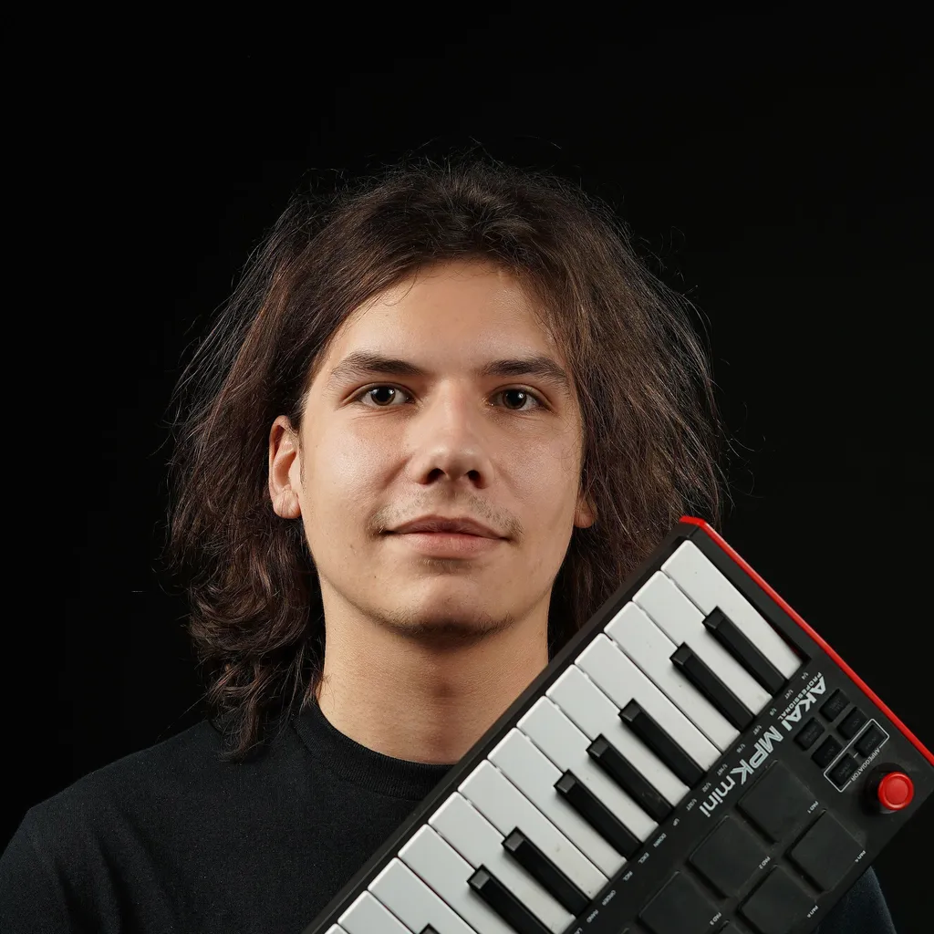 Young man with shoulder length hair holding a MIDI keyboard, set against a black background. The person has a calm expression, conveying a creative mood.