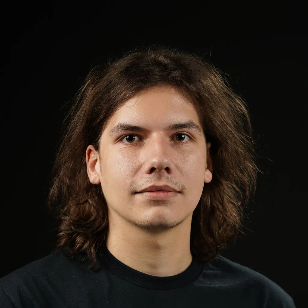 Young man with shoulder-length brown hair, a stubble and a neutral expression, wearing a black shirt.