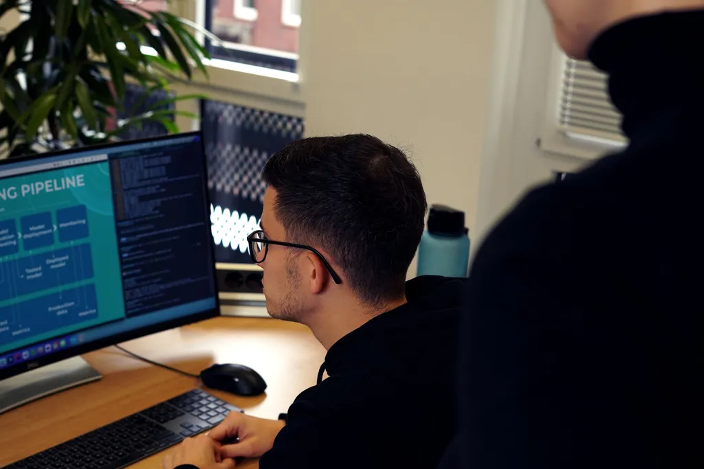 A person working on a computer, while someone else observes their work