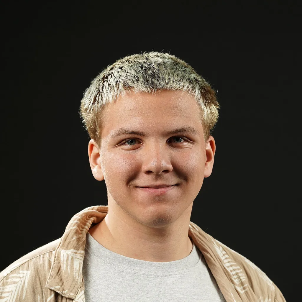 Young man smiling warmly with short, highlighted hair, wearing a light-patterned shirt on top of a gray shirt, set against a black background.