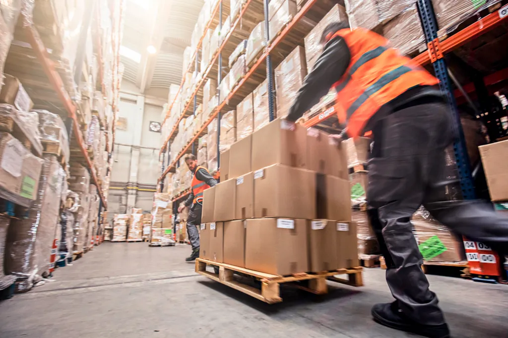 Warehouse worker in hi-vis vest pushing pallet truck loaded with boxes